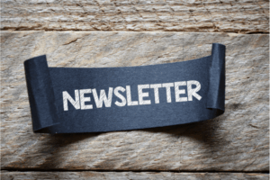 Newsletter written on navy paper curled at edges, with wooden background