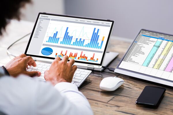 Person typing at keyboard with data charts displayed on computer tablet