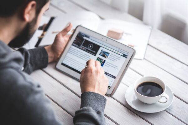 a photo of a man looking a tablet with a cup of coffee.