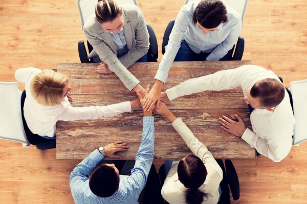 People around a wooden table with hands linked in centre