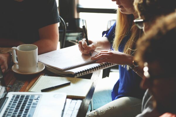 people around table writing in notebook, with laptop and coffee cup on table