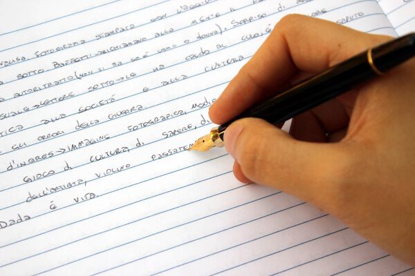 Person holding pen writing on white lined paper