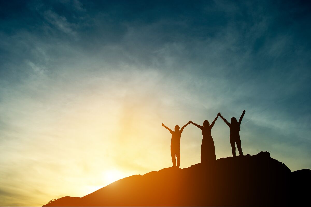 Three people on top of a hill with sunset in background