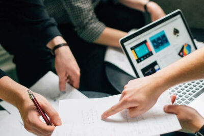 a photo of hands around a laptop and documents