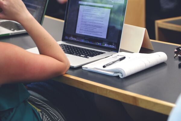 Person sitting a table with laptop open and notebook and pen